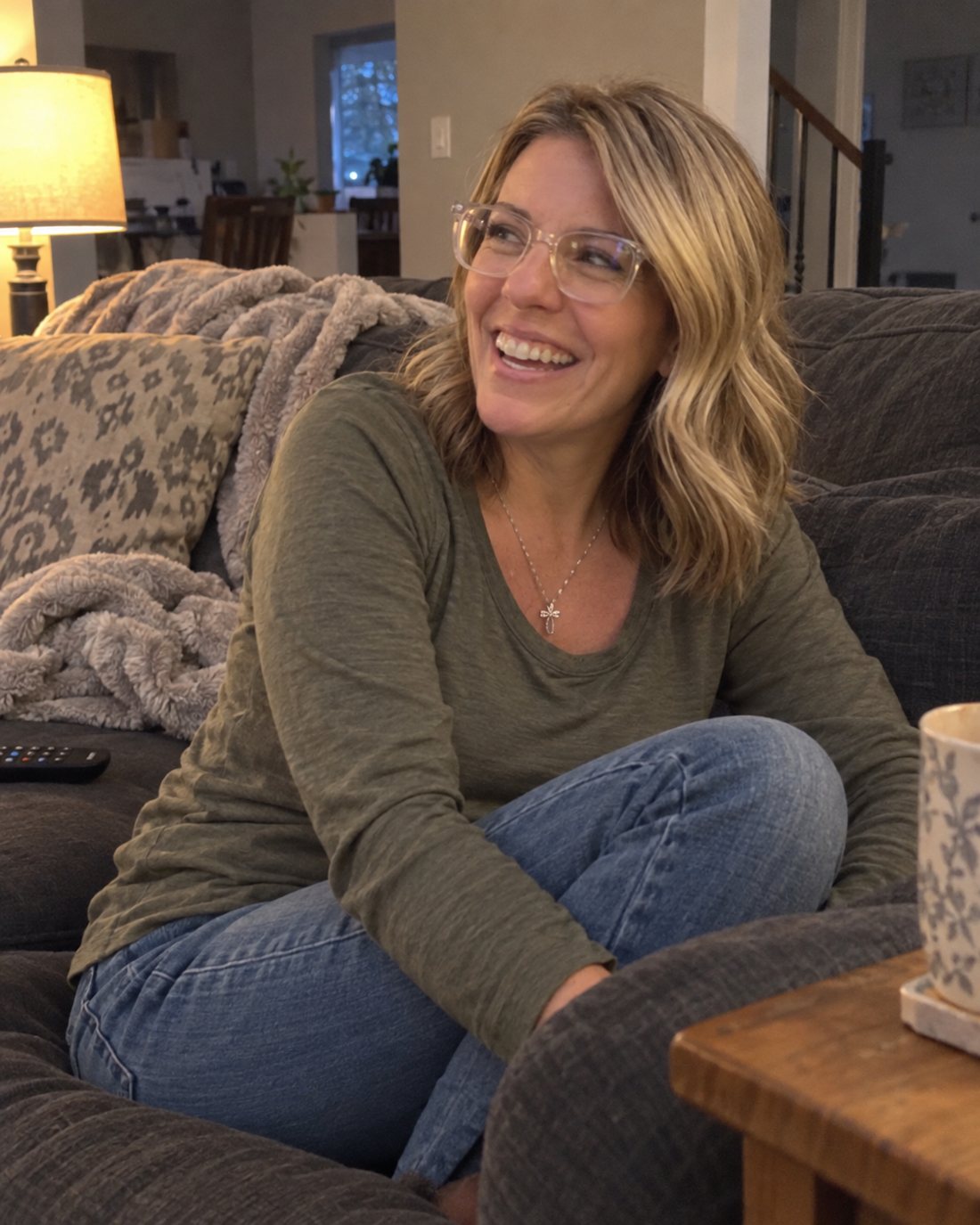 Maureen laughing on the couch with a cup of coffee